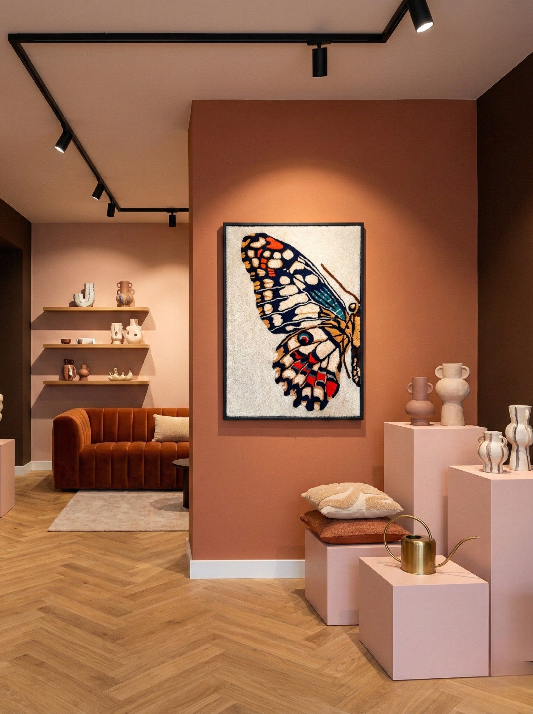 Hand-tufted wall hanging with a close-up butterfly wing in navy, orange, teal and red, displayed on a terracotta wall in a design store setting