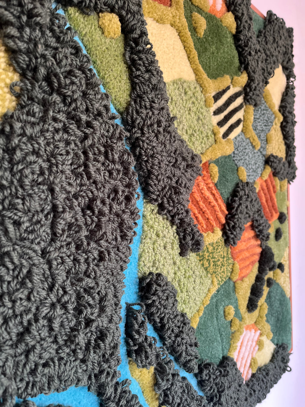 Close-up detail of tufted wall hanging Meadow showing the handmade crocheted dark grey wool border and colorful abstract landscape textures