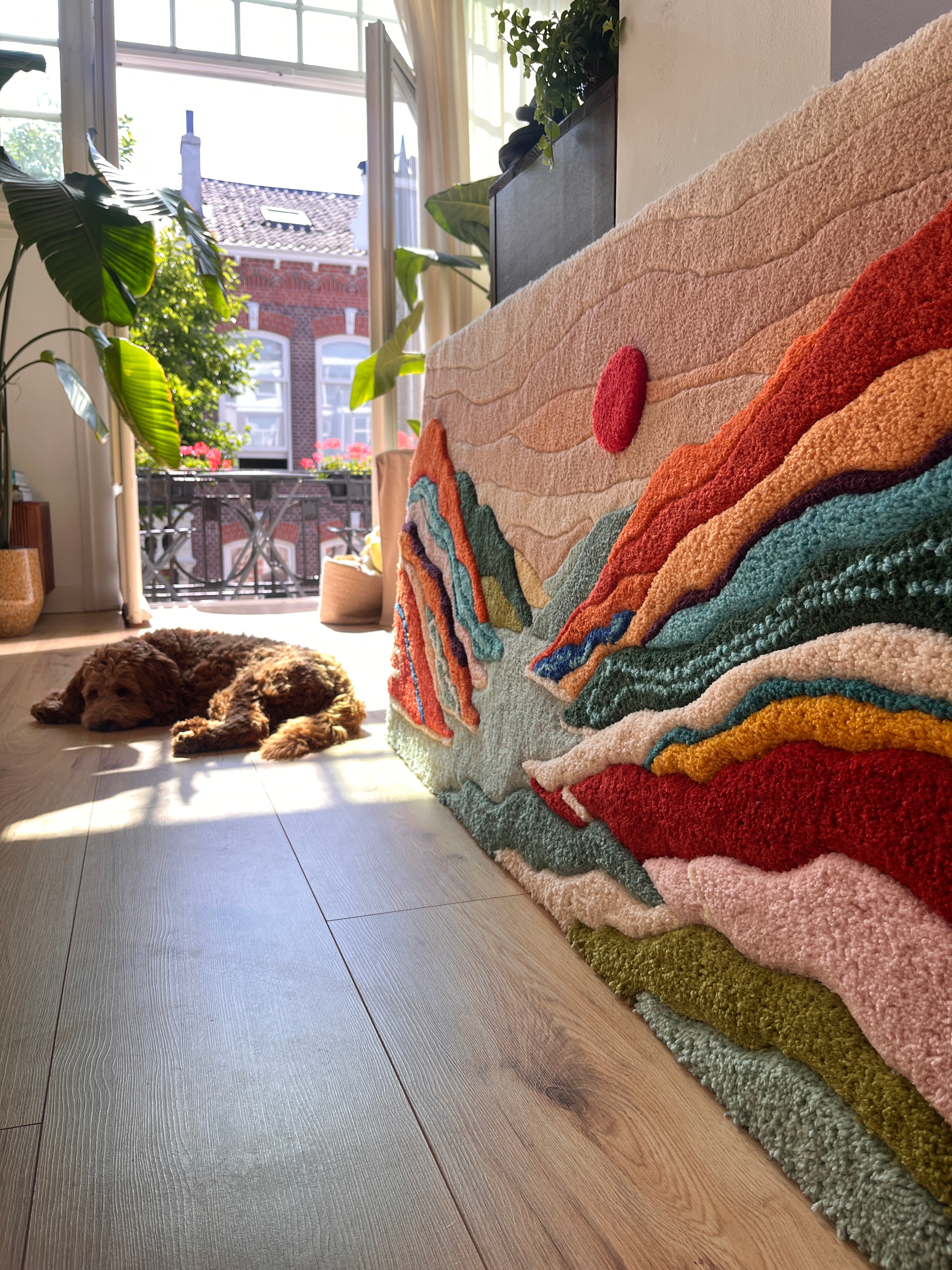 Getuft wandkleed met golvende vormen in petrolblauw, oranje en rood, gefotografeerd in daglicht