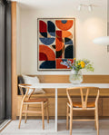 Hand-tufted wall hanging with bold geometric shapes in orange, red and navy blue, displayed above a built-in oak bench in a minimalist dining nook